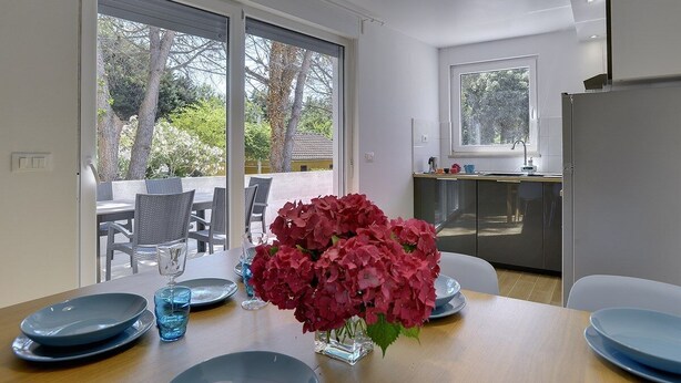 Un'elegante sala da pranzo con un tavolo apparecchiato per due, un vaso di fiori e vista sull'esterno tramite ampie porte scorrevoli.