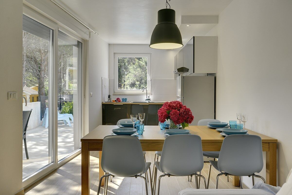 A modern kitchen with a large window, a dining table with chairs, and a hanging light fixture.