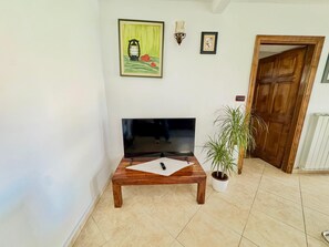 Ein Wohnzimmer mit Flachbildfernseher, Couchtisch aus Holz, Topfpflanze und einer Tür.
