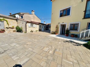 A courtyard with stone paving, a stone building with shutters, and a yellow building with a door and window. - Apartments Barat (73588-A1) - Zminj (Zminj)