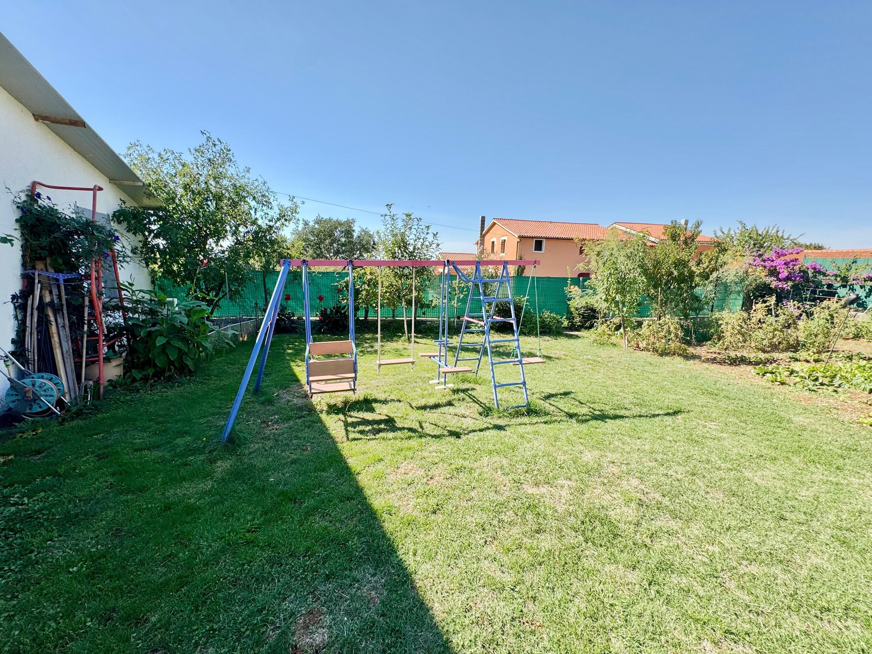 Ein gepflegter Garten mit Schaukel, Kletterleiter und grünem Zaun.