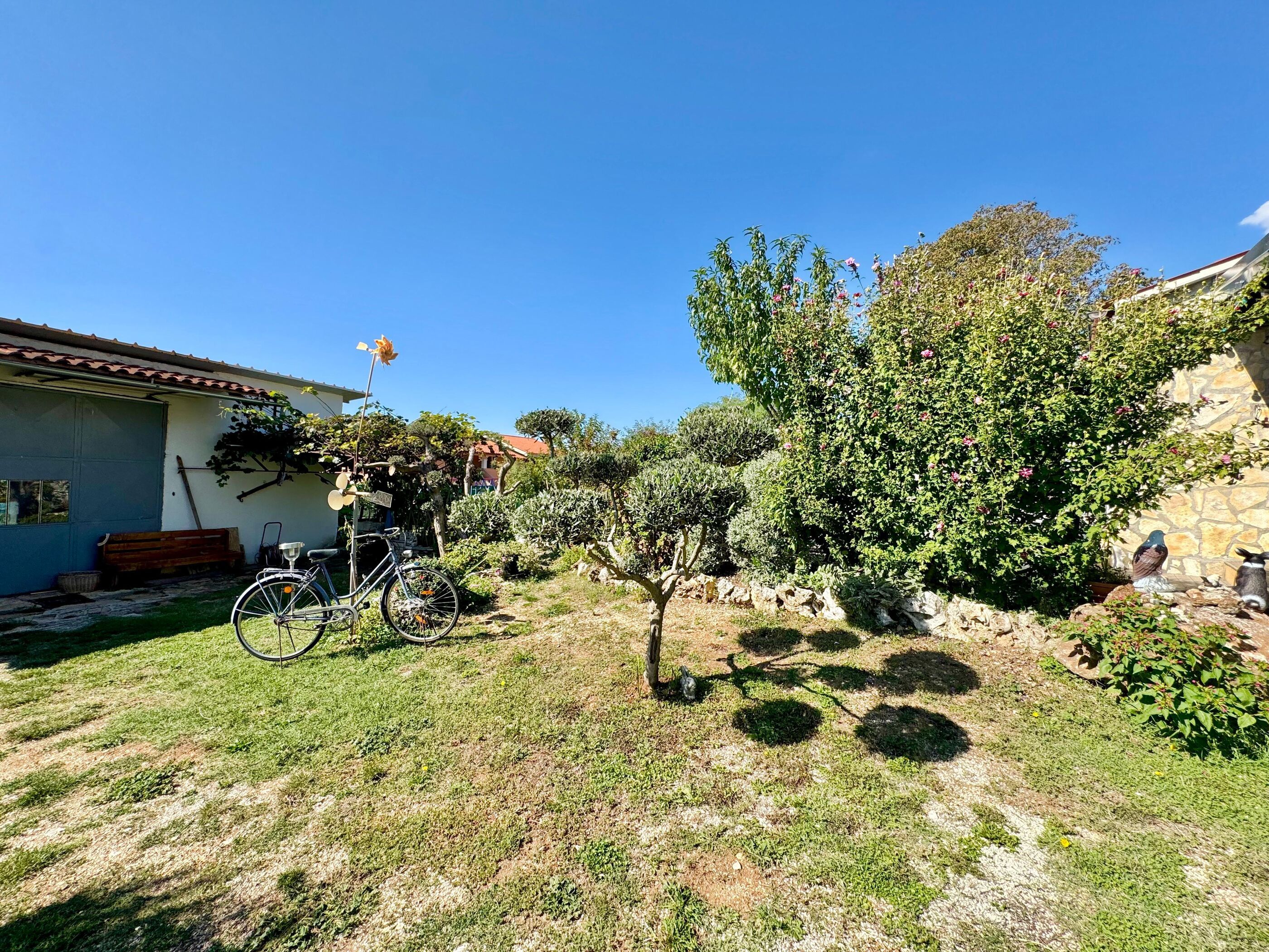 Un jardin avec un vélo, un banc et un mur de pierre.