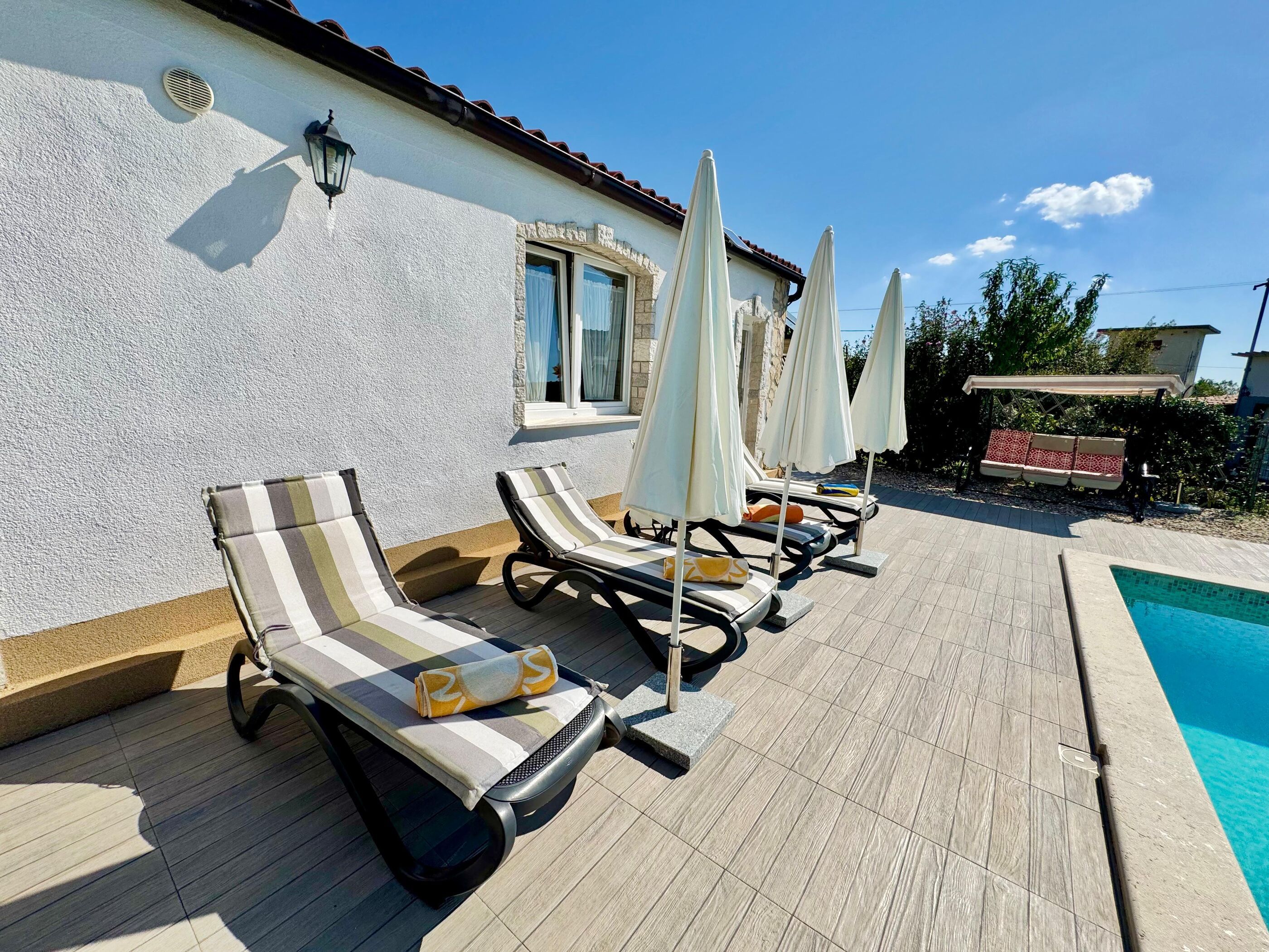 A poolside area with lounge chairs and umbrellas, a tiled deck, and a pool.