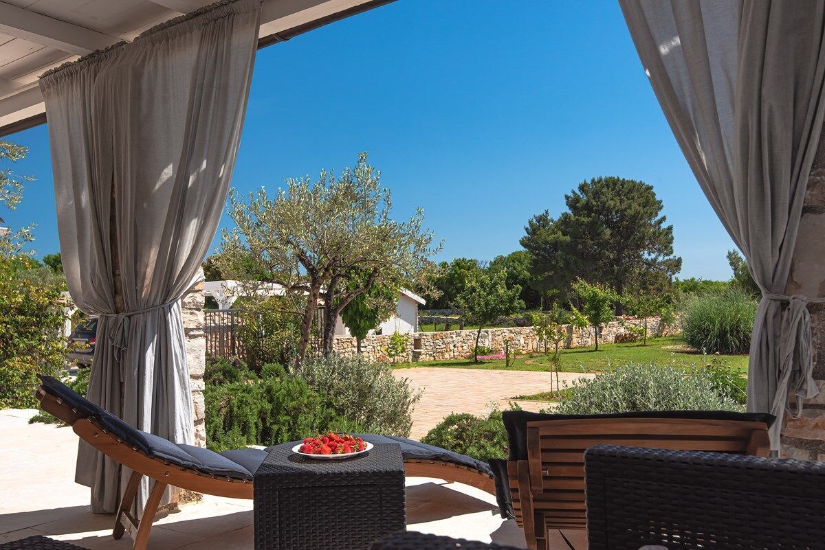Un espace extérieur aménagé avec des meubles en osier, une table sur laquelle est disposée une assiette de fraises, et une vue sur un mur de pierre et de la verdure.