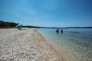 A pebble beach with clear water, a few umbrellas, and a distant shoreline. - Villa Emily (73554-K1) - Peroj (Peroj)