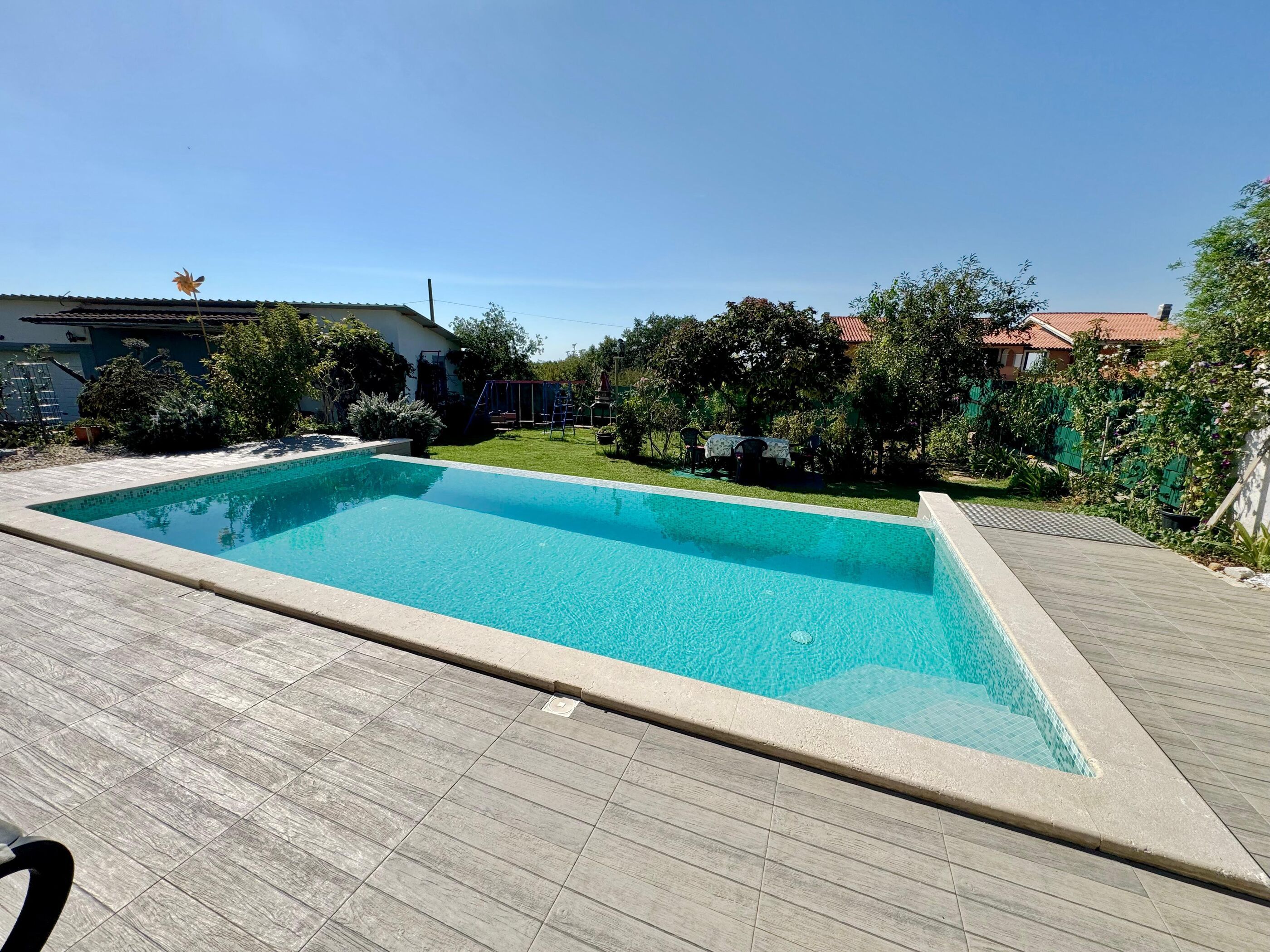 A rectangular swimming pool with a tiled deck surrounding it.