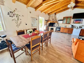 A dining area with a wooden table, chairs, and a red placemat. There is a kitchen area with wooden cabinets and a stone fireplace. - Apartments Barat (73588-A2) - Zminj (Zminj)