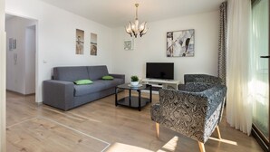Een moderne woonkamer met een grijze bank, een gestreept fauteuil en een televisie op een zwart dressoir.