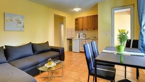 Un espacio habitable compacto con un sofá, una mesa de comedor con sillas, una pequeña cocina y una planta en maceta.