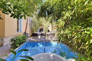 En swimmingpool omgiven av frodig grönska, med utomhusmöbler och en grillplats.