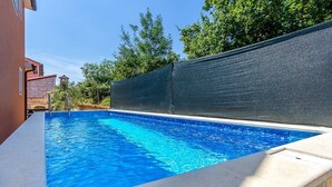 Piscina retangular com água azul cristalina, rodeada por um muro de pedra e um painel preto para privacidade.