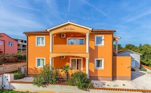 Ein zweistöckiges Gebäude mit Balkon, Namensschild und einem kleinen Anbau.
