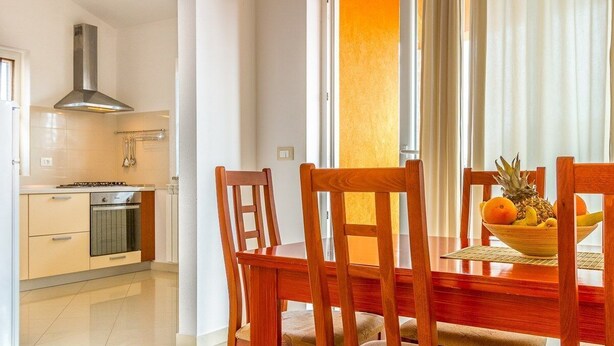 Cozinha moderna com armários brancos, coifa de aço inoxidável e área de refeições com cadeiras e mesa de madeira.