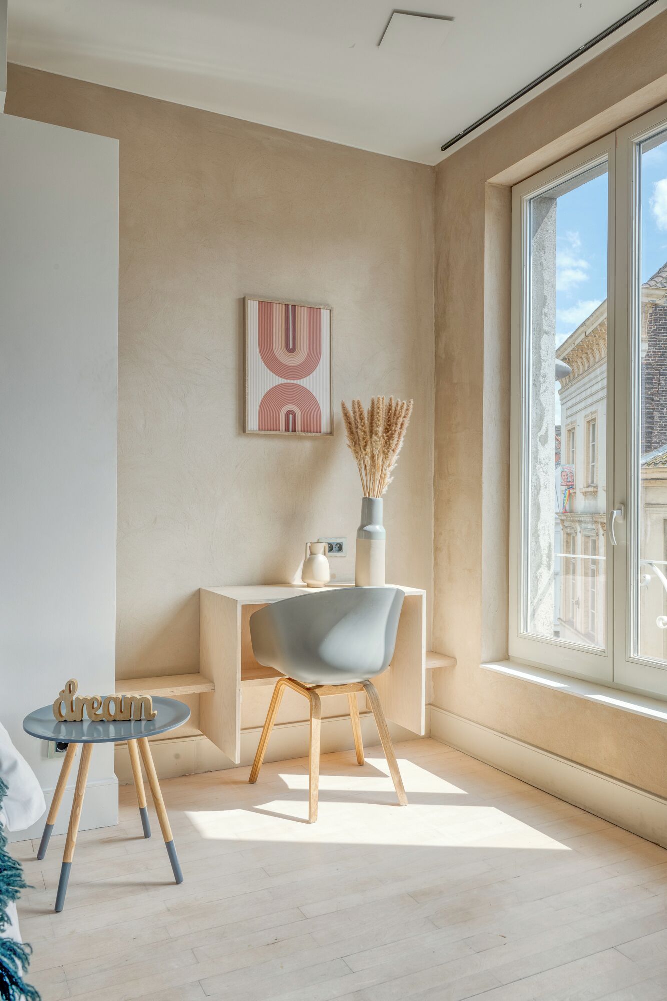 Ein modernes Zimmer mit einem großen Fenster, einem Schreibtisch, einem Stuhl und einer Vase mit Trockenpflanzen.