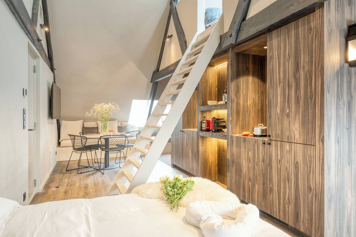Un dormitorio tipo loft moderno con un armario de madera, una escalera y una zona de comedor con mesa y sillas.