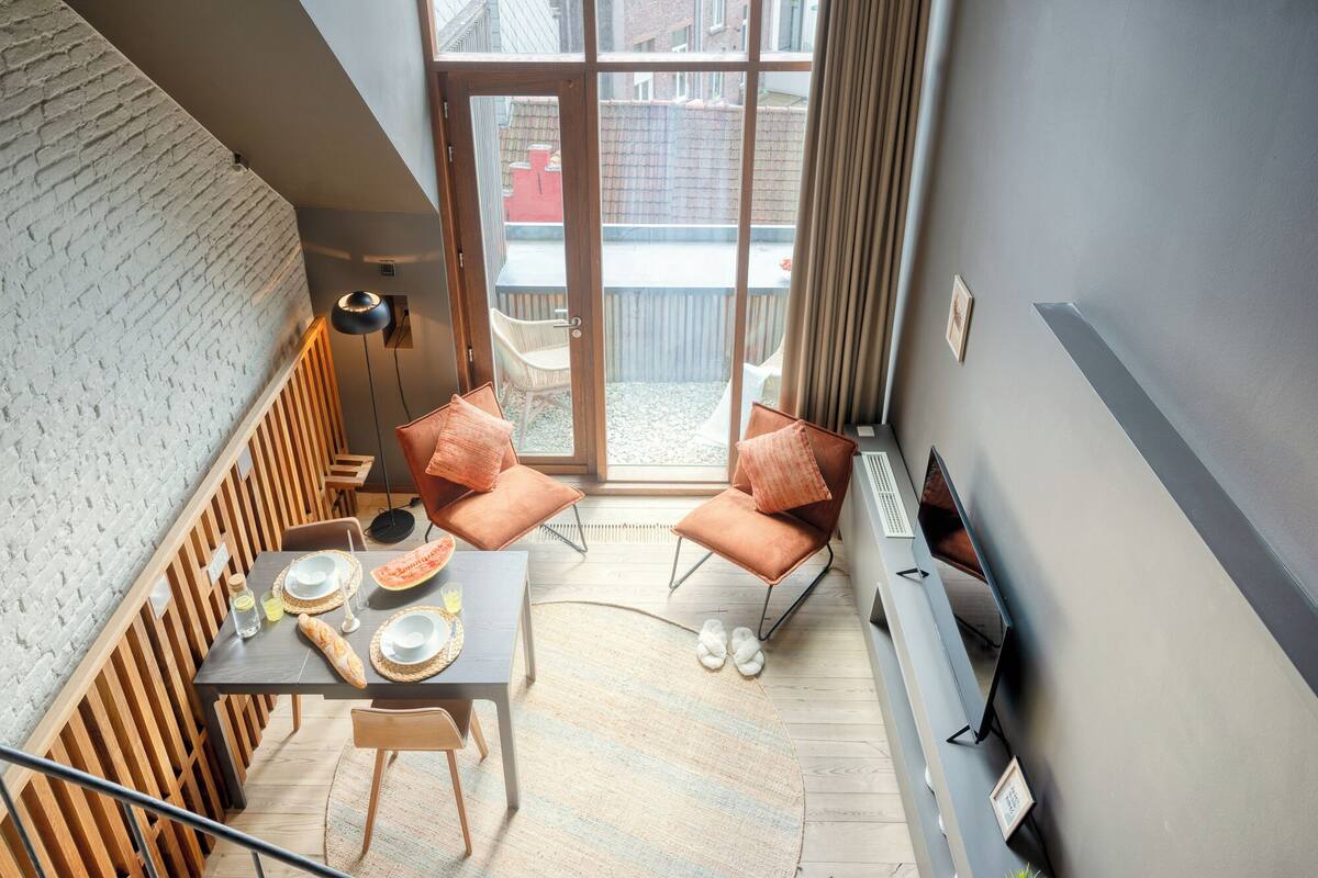 Un interior moderno con zona de comedor, dos sillones acolchados, una mesa con platos, vasos y hogaza de pan.