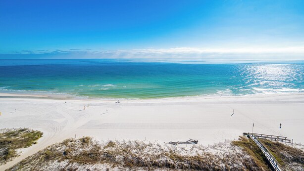 A beach with a clear sky, calm sea, and a sandy shore. - Phoenix V 1411 Gulf Views & Resort Amenities (Orange Beach)
