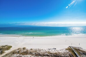 A beach with a clear sky, calm sea, and a sandy shore. - Phoenix V 1411 Gulf Views & Resort Amenities (Orange Beach)