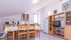 Ett kompakt kök med ett matbord, stolar, ett kylskåp, en mikrovågsugn och en tv placerad på en hylla av trä.
