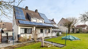 Een huis met zonnepanelen op het dak, een verzorgd gazon en een kleine schuur.