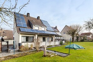 Ein Haus mit Solaranlage auf dem Dach, einem gepflegten Rasen und einem kleinen Gartenhaus.