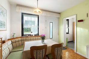 Ein Essbereich mit Tisch, Stühlen, einer Bank, einer Topfpflanze und einem Fenster mit Vorhängen.