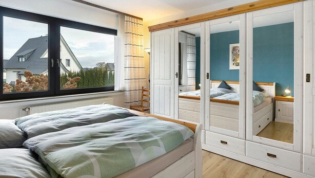 Een slaapkamer met een bed, een kledingkast en een raam met uitzicht op huizen.