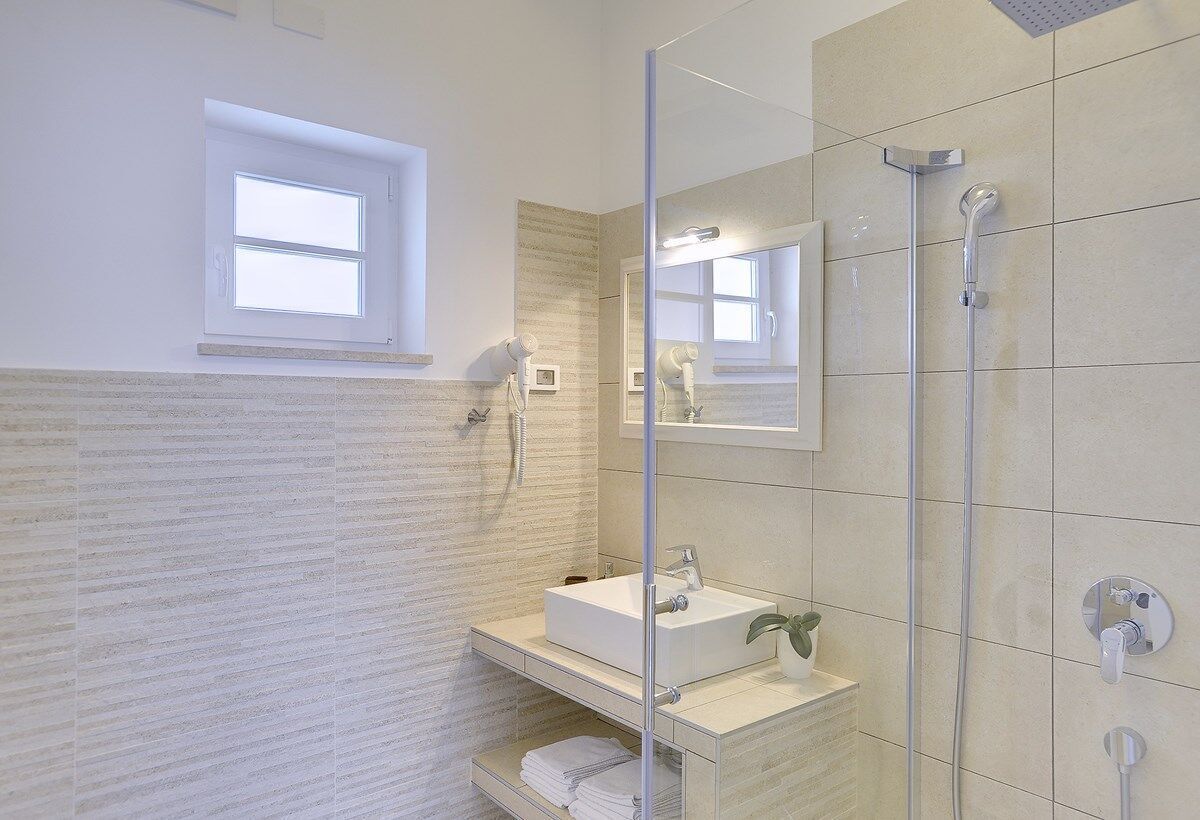 Un baño moderno con cabina de ducha de vidrio, un lavamanos con espejo y una ventana que proporciona luz natural.