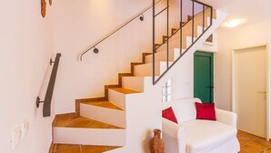 Eine Treppe mit Metallgeländer führt zu einer grünen Tür, ein weißes Sofa mit roten Kissen und ein Blumenvasen steht auf dem Boden.