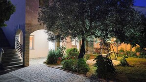 Une cour pavée de pierres, avec un arbre, un escalier et un bâtiment doté d’un toit en tuiles.