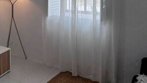 Ein Zimmer mit Stehlampe, einem Fenster mit durchsichtigen Vorhängen und einem weißen Schrank.