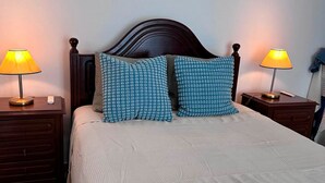 Ein ordentlich bezogenes Bett mit einem gemusterten Kopfkissen, einem Holzkopfbrett und zwei Nachttischlampen.