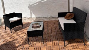 Eine Terrasse mit zwei Korbstühlen, einem kleinen Tisch und einer weißen Wand.