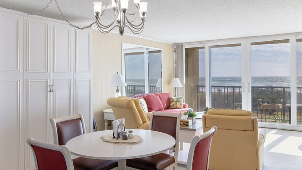 A spacious room with a balcony overlooking the ocean, a dining area with a round table, and a cozy seating arrangement. - Smuggler's Cove 205, 2BR 2BA Oceanfront Condo in Atlantic Beach! (Atlantic Beach)