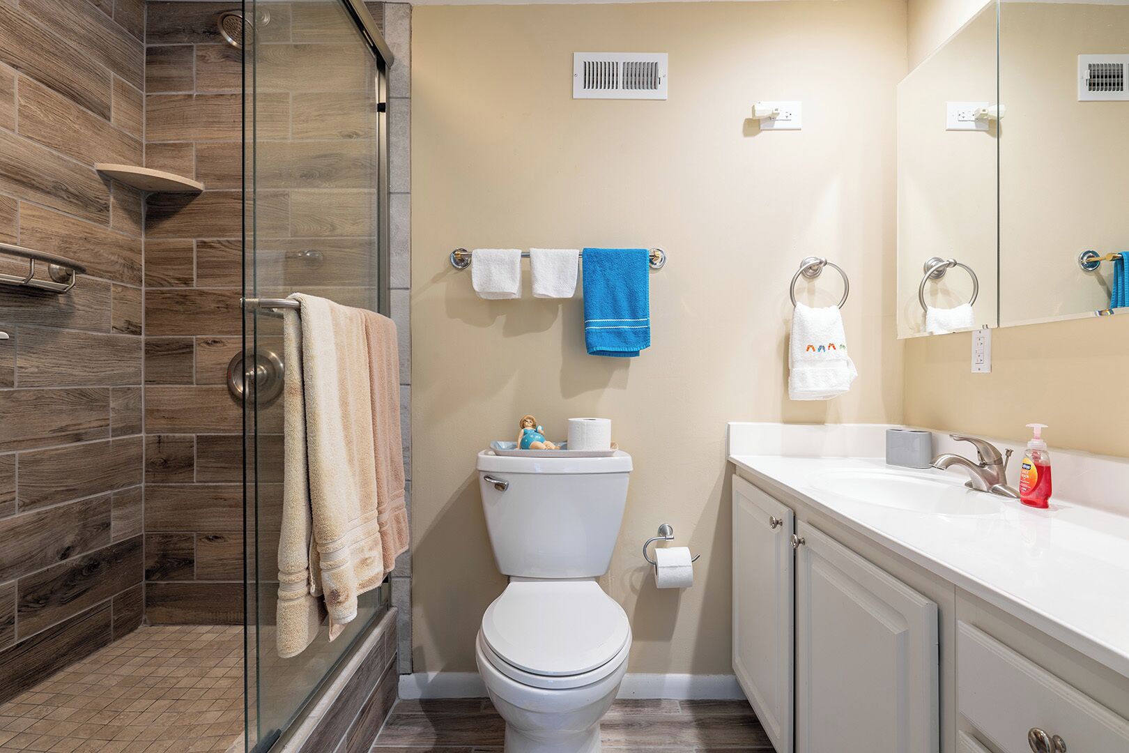 Un bagno con box doccia in vetro, un water, un lavandino con specchio e un portasciugamani con diversi asciugamani.