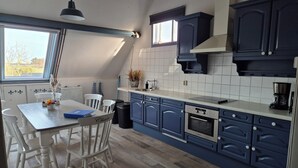Eine Küche mit weißen Schränken, einem Esstisch mit Stühlen, einer Kaffeemaschine und einem Fenster mit Blick auf Bäume.