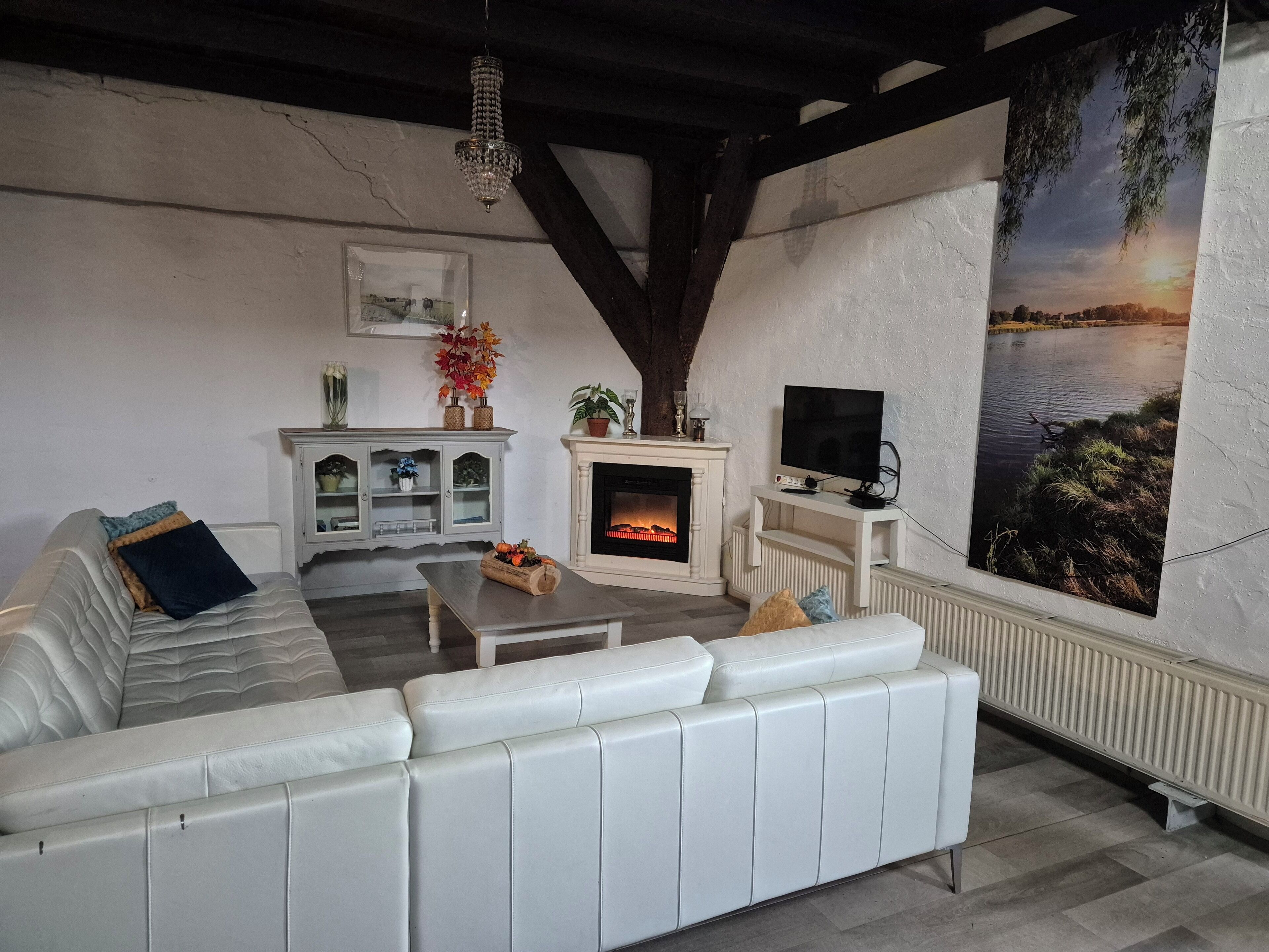 A living room with a white sofa, a fireplace, a television, and a large painting of a sunset over water.