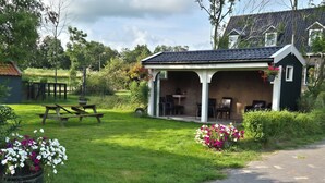 Ein gemütlicher Außenbereich mit überdachter Terrasse, Picknicktisch und Blumenarrangements.