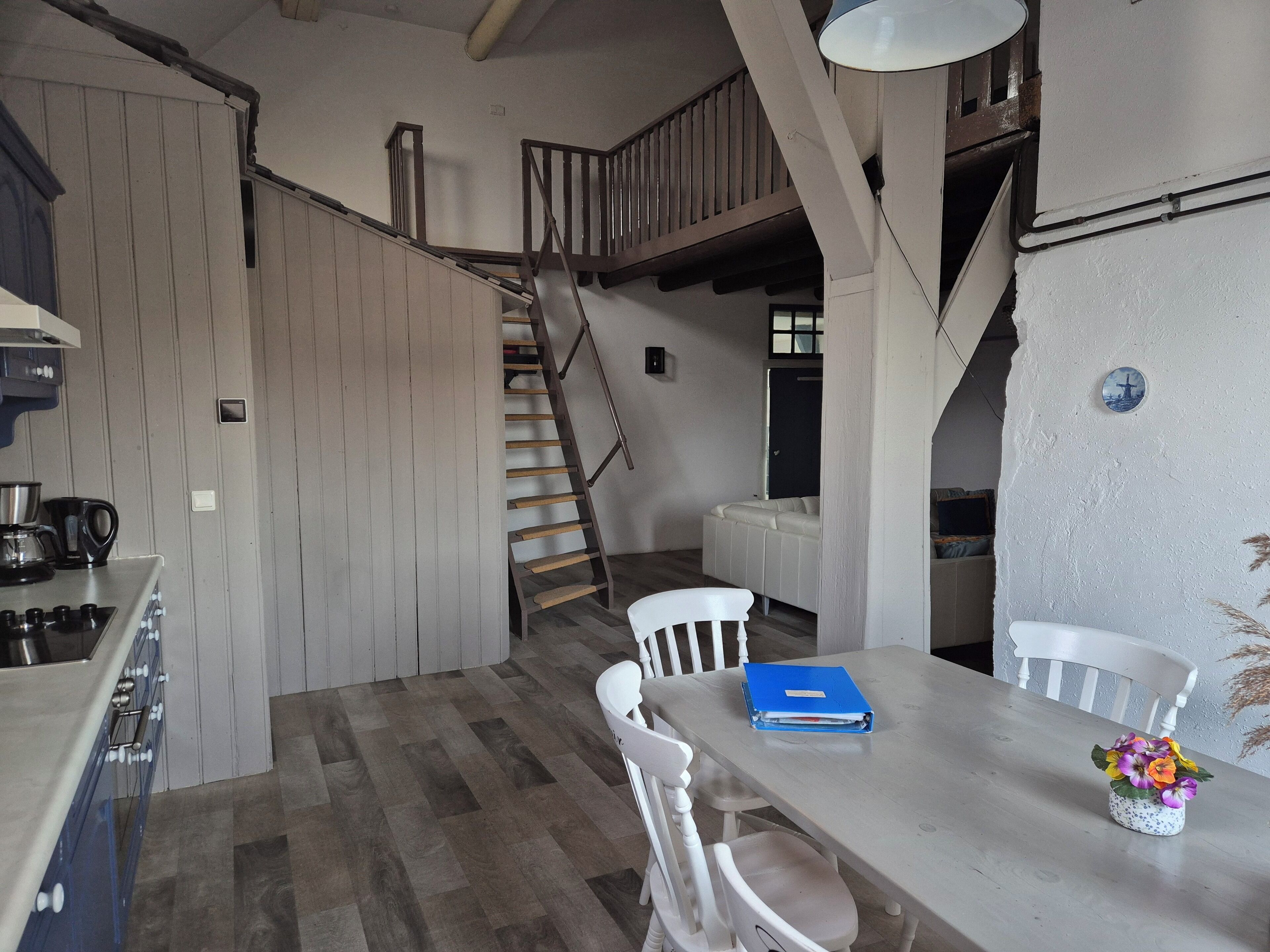 A kitchen with a wooden staircase, a dining table with chairs, and a blue folder on the table.