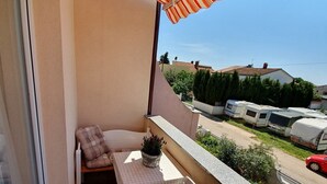 Een balkon met een gestreepte luifel, een tafel met een geruit tafelkleed, twee comfortabele stoelen en een bloempot met plant.