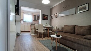 Een moderne woonkamer met een bruine bank, een eettafel met stoelen, en een keuken op de achtergrond.