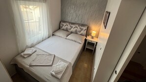 Una camera da letto con un letto, un comodino con una lampada e una finestra con tende leggere.