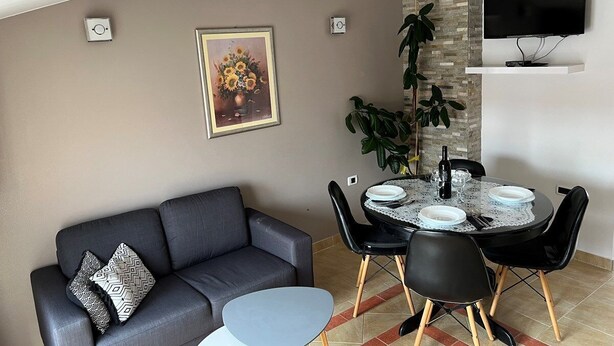 Un soggiorno moderno con un divano grigio, un tavolo da pranzo rotondo con sedie nere e una TV a parete.