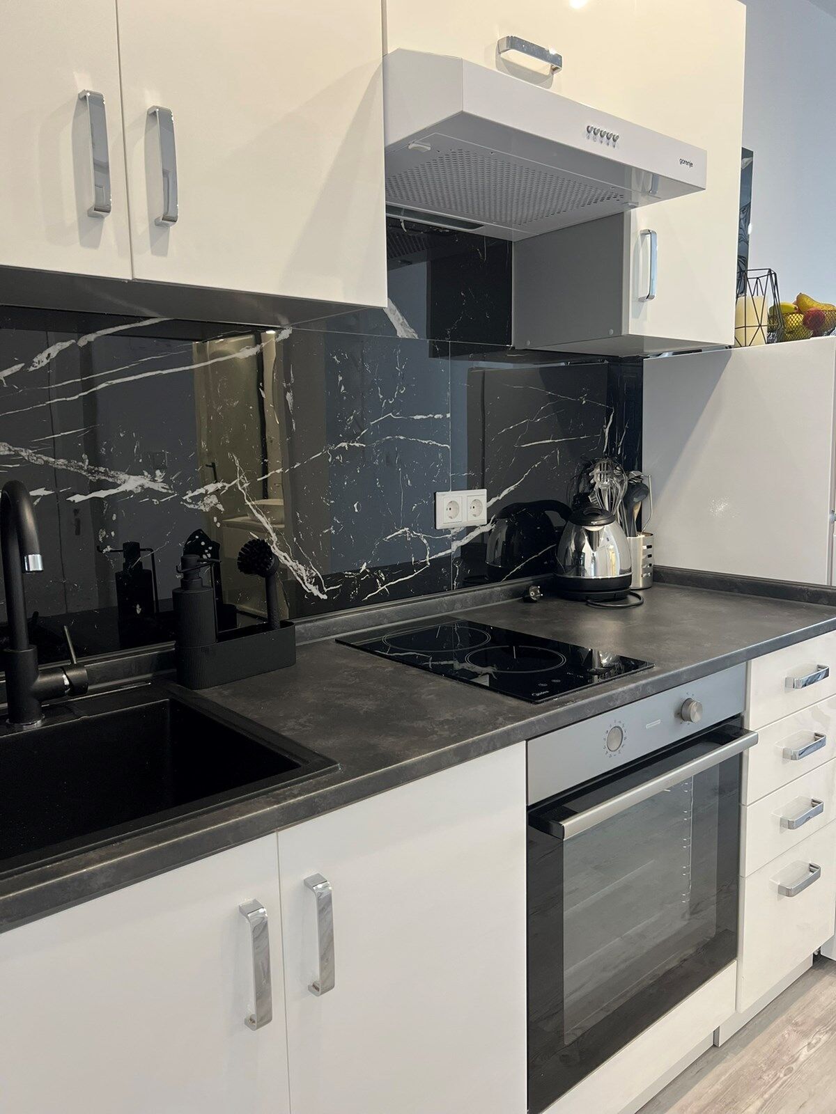 A modern kitchen with white cabinets, a black countertop, and a built-in oven.
