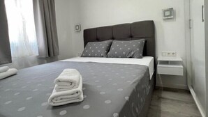 A neatly made bed with a grey polka dot bedspread and pillows, a bedside table with a lamp, and a window with curtains. - Apartments Vuletic (73661-A3) - Medulin (Medulin)