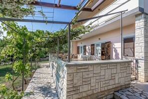 A stone patio with a pergola, outdoor seating, and a view of a building with a stone facade and windows. - Apartment Anamarija (73672-A1) - Medulin (Medulin)