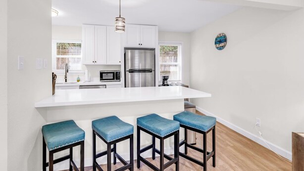 A modern kitchen with white cabinets, stainless steel appliances, and a central island with bar stools. - Porter Condos (Ocean Springs)