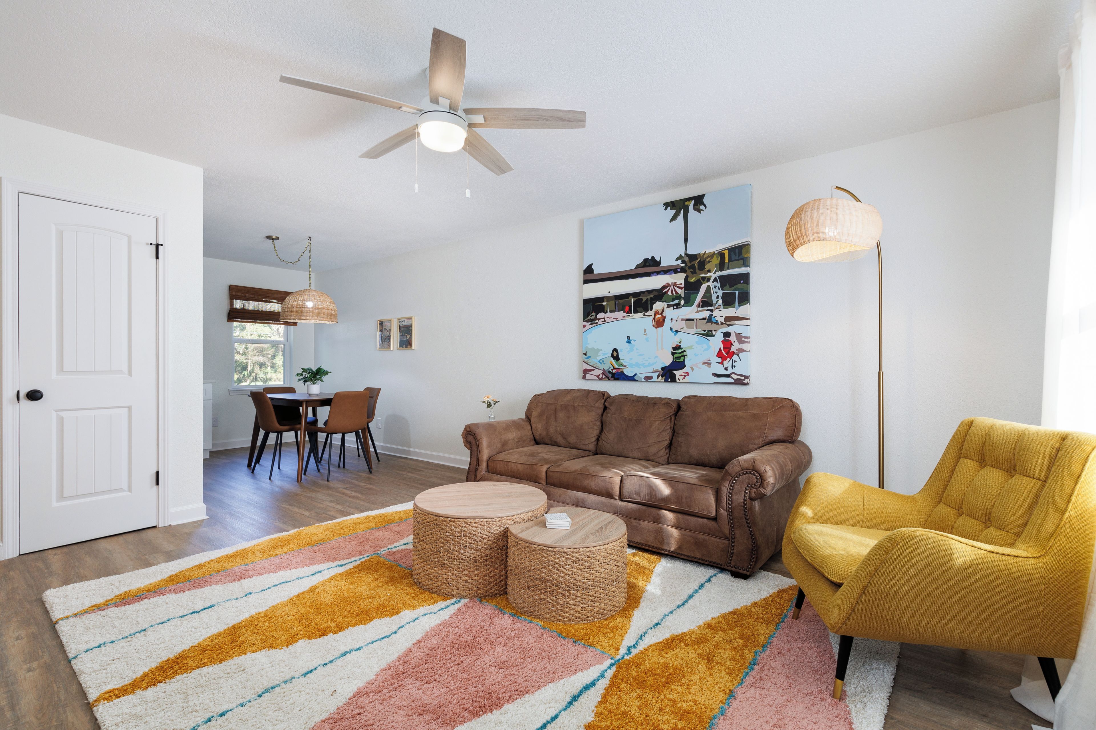 Un salon avec un canapé en cuir marron, un fauteuil jaune, un ventilateur de plafond et un tableau accroché au mur.