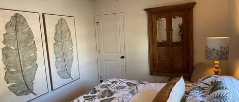 A bedroom with two single beds, a ceiling fan, a wooden cabinet, and two leaf-patterned wall art pieces.