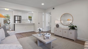 A modern living room with a sofa, coffee table, and a dining area with a refrigerator and cabinets. - Porter Condos (Ocean Springs)